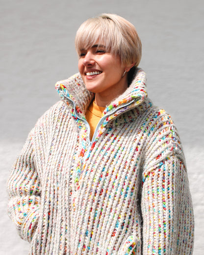 Pattern Designer smiling while wearing a size MEDIUM Brioche Crochet Pullover in the fruity-pebbles colorway. Statement collar is shown half zipped layered over an orange shirt for a layered look in a joyful colorway. 