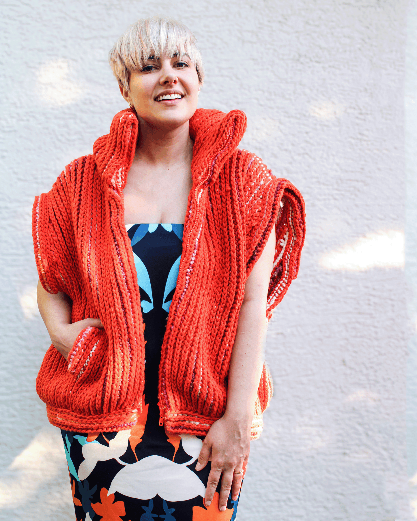 Brioche Crochet Vest — worn open-front with separating zipper undone over a layered outfit in Sherbet colorway on size medium designer, sleeveless two-ways-to-wear unisex styling with faux-welt pockets visible.